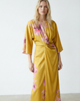 Robe midi croisée satinée jaune à fleurs roses, col V et manches larges, vue de face en lumière naturelle