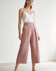 Femme en pantalon court plissé taille haute ceinture élastique à poches rose, projetant un look détendu et stylé tout en marchant avec assurance. Pantalon plissé femme.