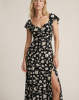 Femme dans une robe longue noire à imprimé floral fendue côté élégante, soulignant son allure chic et féminine avec la robe avec fente latérale.