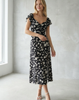 Femme élégante portant une robe longue noire à imprimé floral avec fente latérale, idéale pour des occasions spéciales et un look sophistiqué.