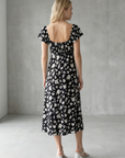Femme de dos en robe longue noire à imprimé floral fendue sur le côté élégante, parfait pour compléter un look d'été avec la robe avec fente latérale.