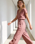 Femme marchant avec grâce dans un pantalon court plissé taille haute ceinture élastique à poches de couleur rose, affichant une allure moderne et élégante. Pantalon plissé femme.