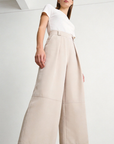 Femme portant un pantalon court plissé taille haute ceinture élastique à poches dans une teinte beige, affichant un style à la fois chic et confortable. Pantalon plissé femme.