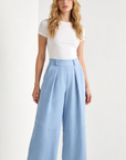 Femme debout dans un pantalon court plissé taille haute ceinture élastique à poches, mettant en avant un style chic et moderne. Pantalon plissé femme.