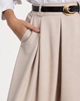 Détail du pantalon fluide taille haute femme en beige, avec une chemise blanche, présentant des plis élégants et une ceinture stylée.