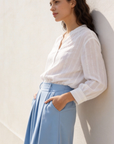Femme avec un pantalon fluide taille haute femme bleu et une chemise blanche, posant contre un mur, look décontracté et élégant.