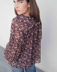 Femme portant une blouse semi-transparente coupe fluide noire voile léger avec imprimé floral, idéale pour un style décontracté. Blouse fleurie femme.