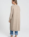 Modèle montrant le dos d'un cardigan long femme beige, avec une coupe ample et douce, idéal pour un style décontracté.