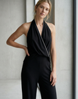 Femme montrant la combinaison halter noire à nœud, dos nu et jambe large, parfaite pour un look de soirée sophistiqué en combinaison noire élégante femme.
