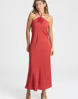 Modèle portant une robe midi halter fluide en viscose rouge, avec des escarpins, parfaite pour les occasions spéciales.