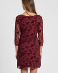 Femme de dos enrobe courte dentelle chic manches 3/4 bordeaux, dévoilant la délicatesse de la dentelle. Un choix élégant pour un look de soirée, robe courte dentelle.