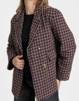 Femme avec un blazer coton femme bordeaux et marron, coupe élégante, posant avec une main sur la taille, révélant le design structuré du vêtement