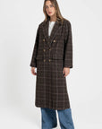 Femme portant un manteau long croisé marron en coton mélangé, présentant une silhouette élégante avec des boutons, parfaite pour le quotidien. Manteau long croisé femme en coton mélangé marron.