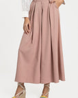 Femme en pantalon fluide taille haute femme rose, avec une blouse blanche, posant avec élégance et naturel.