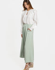 Femme stylée avec un pantalon fluide taille haute femme vert menthe, portant une blouse blanche, look frais et élégant.
