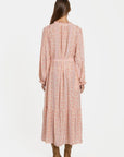 Vue arrière d'une femme dans une robe longue fluide imprimée avec ceinture rose, soulignant sa coupe fluide et élégante.