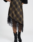 Gros plan d'une jupe midi satinée asymétrique en satin, mettant en avant le motif tartan et la délicate finition en dentelle.