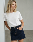 Femme portant une mini jupe en jean tendance, coupe courte, associée à un t-shirt blanc pour un look décontracté.