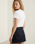 Vue arrière d'une femme en mini jupe en jean, montrant une silhouette moderne avec un t-shirt blanc.