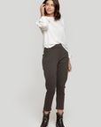 Femme souriante portant un pantalon fluide taille haute gris avec un haut blanc, pour un look décontracté.