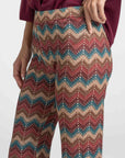Gros plan sur le pantalon flare taille haute fluide imprimé en zigzag multicolore porté par une femme.