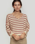 Modèle portant un pull court femme en maille torsadée col V style cropped avec des rayures bordeaux et crème.