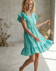 Robe fluide manches courtes en polyester légère — coupe féminine, modèle turquoise, femme souriante, dans une ambiance naturelle.