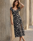 Modèle portant une robe longue noire à imprimé floral fendue sur le côté élégante, mettant en valeur le style romantique de la robe avec fente latérale.