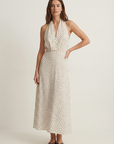 Femme debout dans une robe midi imprimée écru à pois, col halter décolleté plongeant, sur fond neutre.