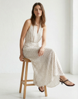 Femme assise dans une position décontractée portant une robe midi imprimée écru à pois, col halter décolleté plongeant.