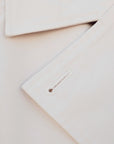 Détail du tissu d'un trench coat court femme beige à double boutonnage, soulignant la qualité et le design élégant de la pièce.