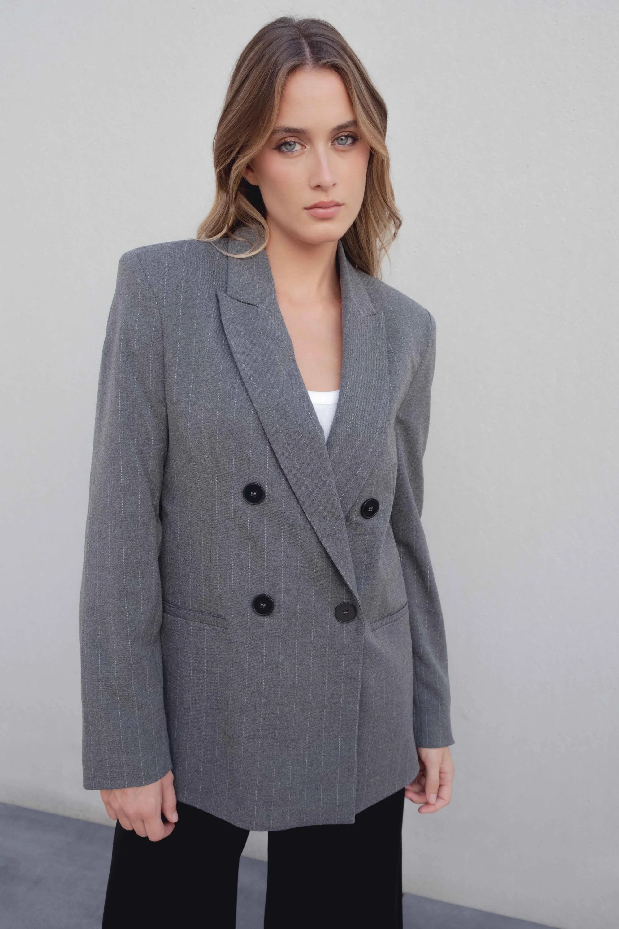 Femme en pose avec un blazer femme chic gris à rayures fines et un look professionnel, idéal pour les occasions formelles.