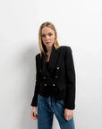 Femme portant une veste blazer noir femme boutonnée à double poitrine, associée à un pantalon décontracté, idéale pour un look moderne et élégant.