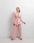 Femme posant avec style dans un Blazer Rose Femme Ceinturé, accompagné de pantalon assorti pour un look harmonieux.