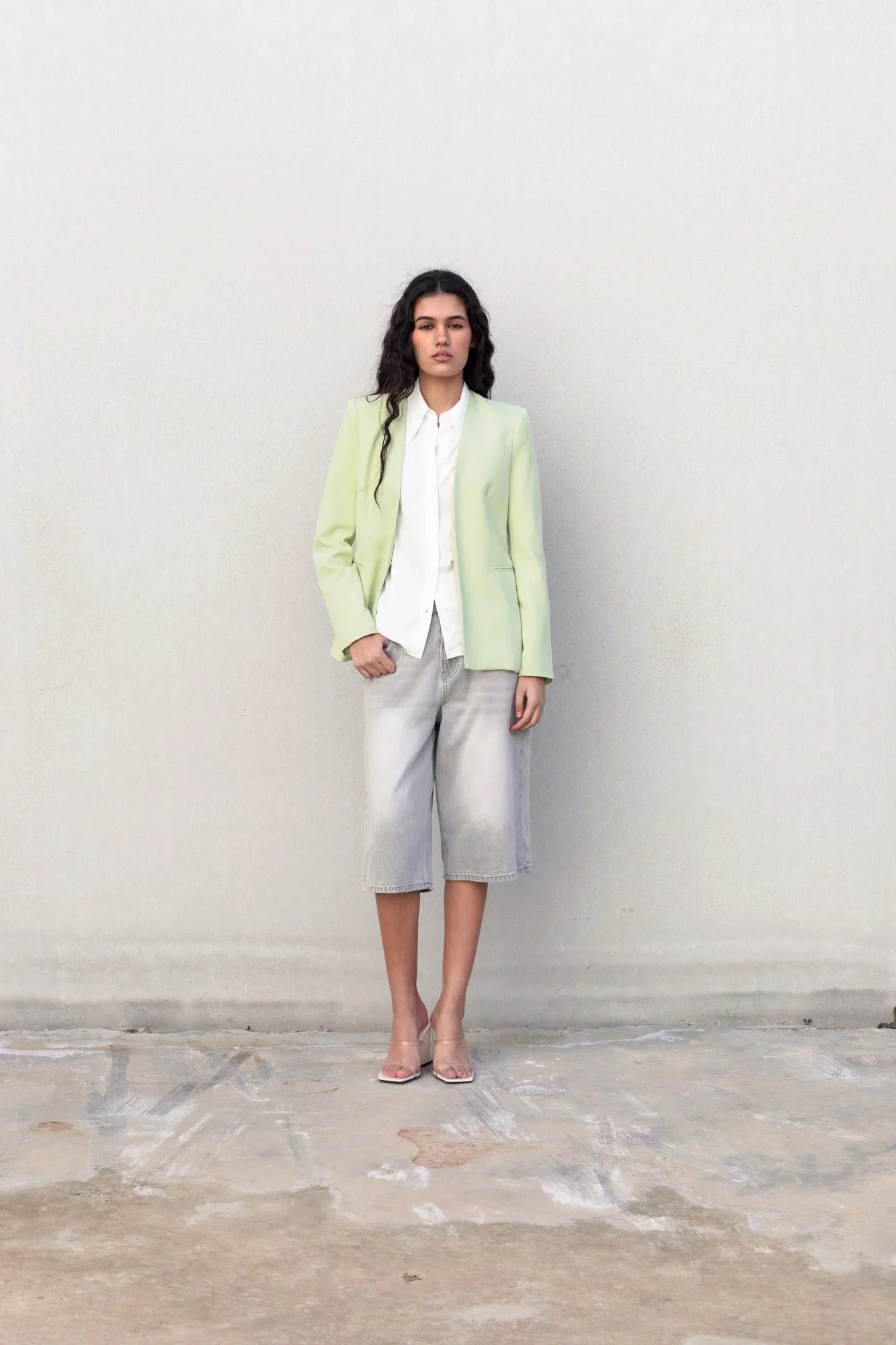 Femme en blazer sans rabat vert clair, chemise blanche, shorts gris, talons transparents