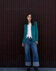 Femme portant un blazer vert ajusté sans col, parfait pour toutes les occasions, associé à une blouse blanche et un jean décontracté. Idéal pour un style chic et contemporain.