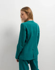 Femme vue de dos dans un blazer vert femme ajusté sans col, avec un pantalon coordonné, mettant en avant le confort et le style moderne.