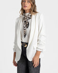 Femme présentant un blazer femme chic blanc, associé à un foulard élégant pour ajout de style.