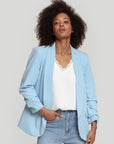 Femme dans un blazer femme chic bleu clair, avec un haut décontracté et un jean.
