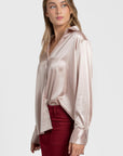 Vue latérale d'une blouse satinée femme élégante, à col chemise, porté par un modèle qui affiche un style chic avec une jupe rouge.