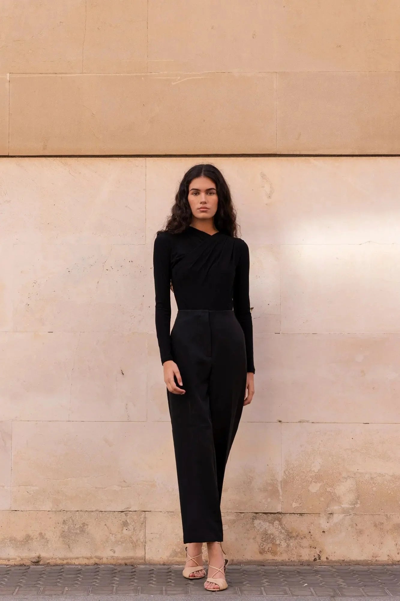 Femme portant le body drapé noir asymétrique avec top noir et talons ouverts pâles