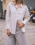 Détail de la chemise ample femme à fines rayures blanc et beige portée par une femme, montrant le tissu fluide et les manches longues.