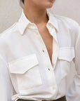 Détail de la chemise blanche en soie à poches pour femme, mettant en valeur les boutons et le tissu léger, idéale pour un style décontracté.