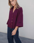 Vue de profil d'une femme portant une chemise élégante bordeaux à boutons dorés, mettant en avant les détails tendance de la coupe ample. Parfaite pour un style élégant en tant que chemise bordeaux femme.