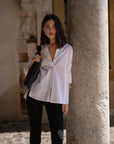 Chemise Femme Blanche Ample en popeline, portée par un modèle devant un pilier dans un cadre urbain élégant.