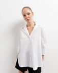 Chemise Femme Blanche Ample en popeline, avec un modèle posant en studio, mettant en avant le design chic.