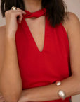 Haut rouge femme chic col noué, décolleté profond pour un look élégant, porté par une femme montrant son accessoire.