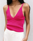 Femme portant un pull crop top fuchsia en maille côtelée à décolleté V profond et bretelles fines, accompagné de pantalons clairs.