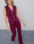 Femme en pose dynamique montrant le débardeur tricot femme bordeaux à boutons dorés, soulignant le style et la coupe ajustée.