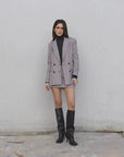 Modèle en pose portant le blazer femme double boutonnage à carreaux avec mini jupe élégante de Sapiato et bottes noires.